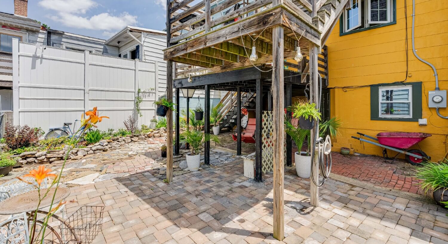 Backyard of a home showing a wood deck, hanging chairs, potted plants and a red wheelbarrow