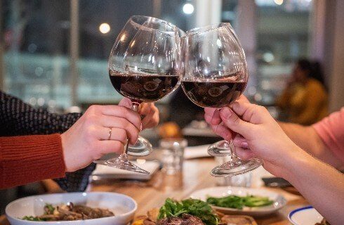 Four people holding clear glasses half-full of red wine over a dinner table