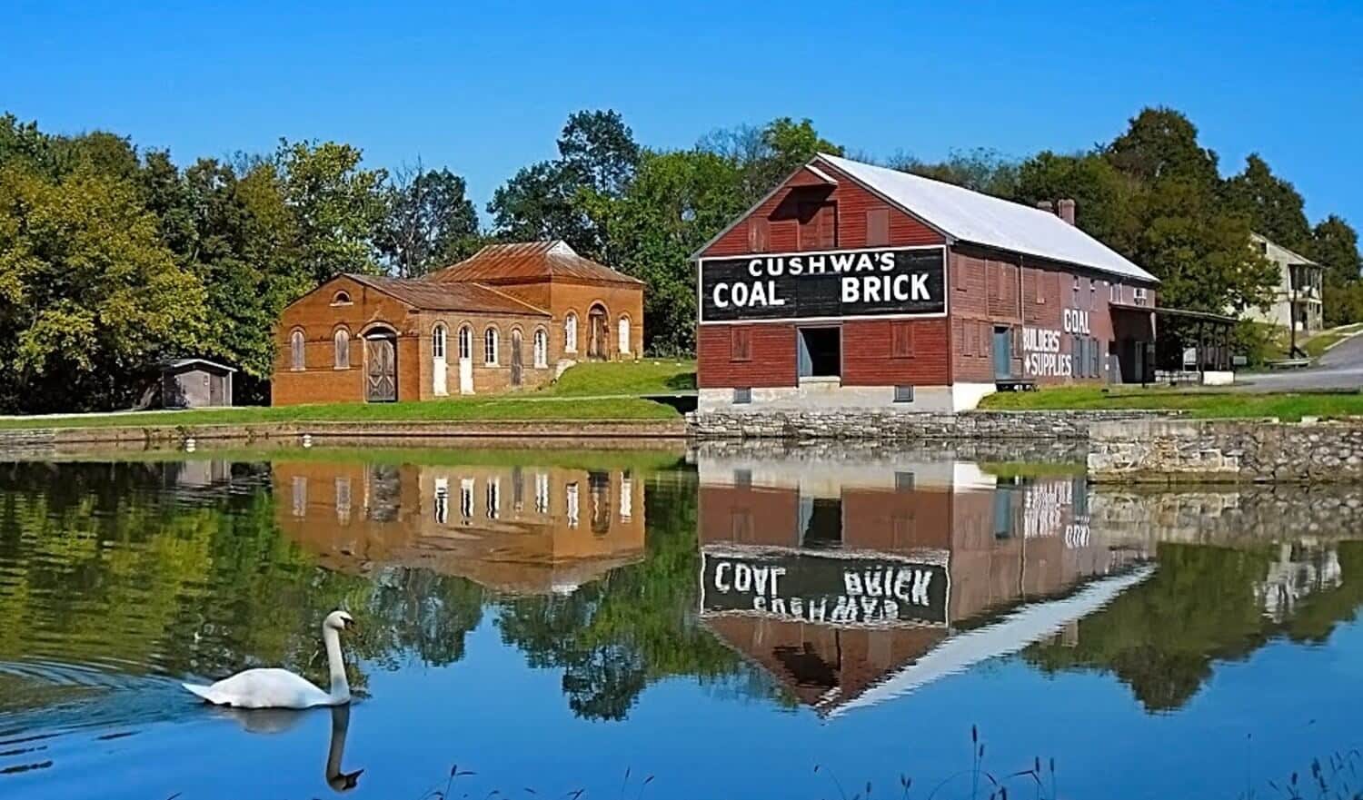 	Two old buildings sitting near a pond of water with one white swan swimming