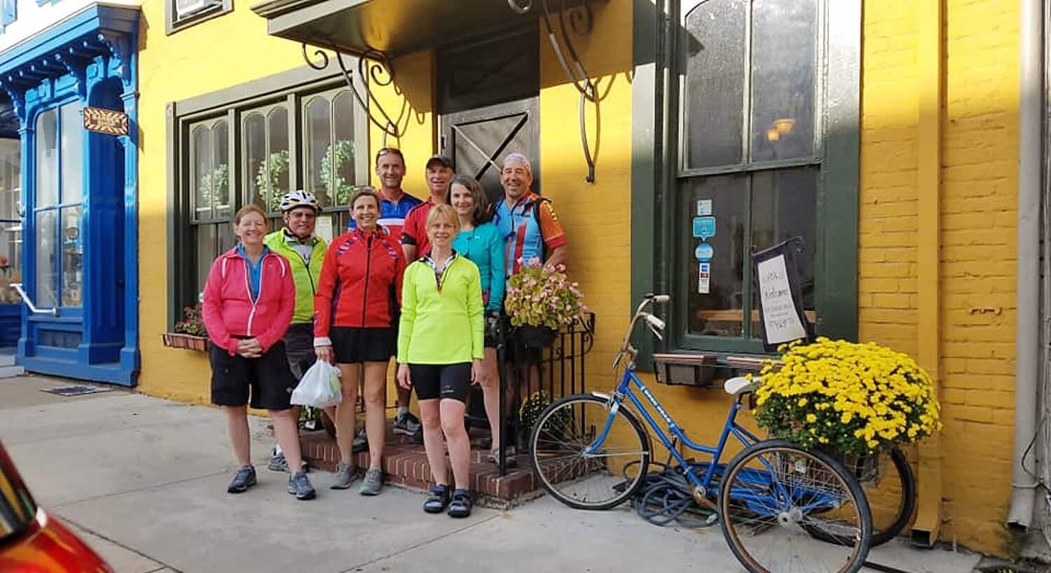 A group of people in cycling gear standing in front of a home with yellow brick