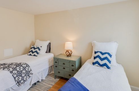 Guest room with two twin beds in white and blue linens with a green dresser and lamp in between