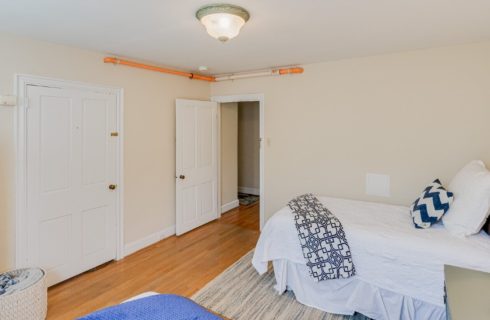 Spacious bedroom with two twin beds, tall green armoire and open door leading to a hallway