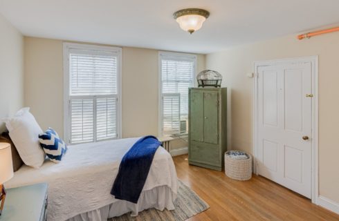 Bright bedroom with a twin bed, green armoire, closet door and two windows