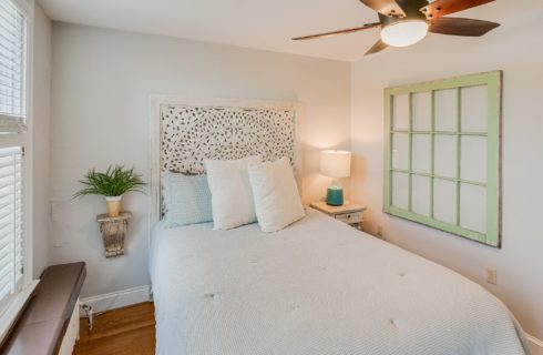Cozy bedroom with queen bed, decorative headboard, frame artwork and ceiling fan