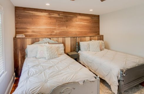 Bedroom with two full size beds in white linens in front of unique wood feature wall