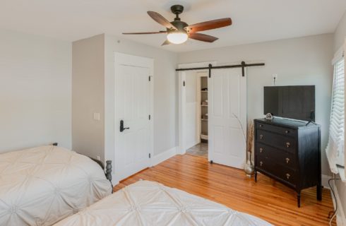 Bedroom with two full size beds, hardwood floors, dresser with TV and slider barn door
