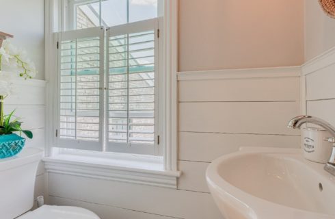 Bathroom with white shiplap detail, pedestal sink and bright window with shutters