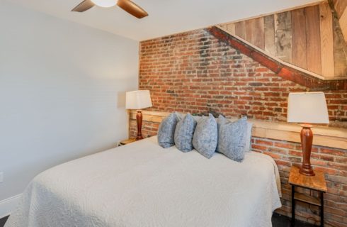 Bedroom with queen bed, brick and wood featured wall and side tables with lamps
