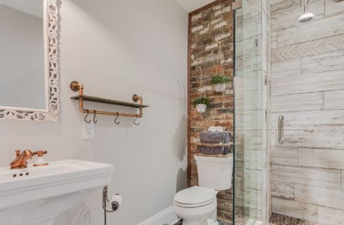 Bathroom with pedestal sink, glass door shower and toilet in front of brick wall detail