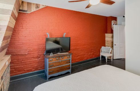 Bedroom with bright orange brick wall, king bed and rustic wood paneled walls