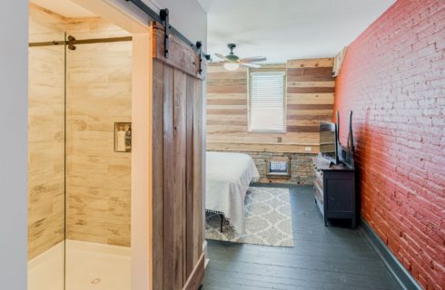 Hallway of a bedroom with brick and wood wall features. and bathroom with barn door slider