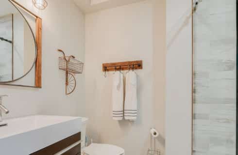 Bathroom with glass shower walls, white vanity with circular mirror and white hanging towels