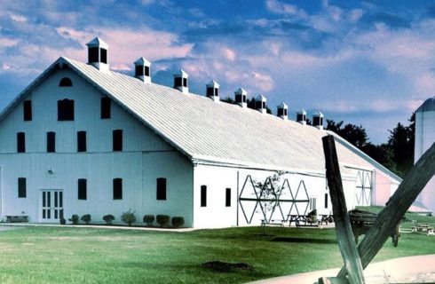 Large white barn with black windows and tall silo next to grassy area