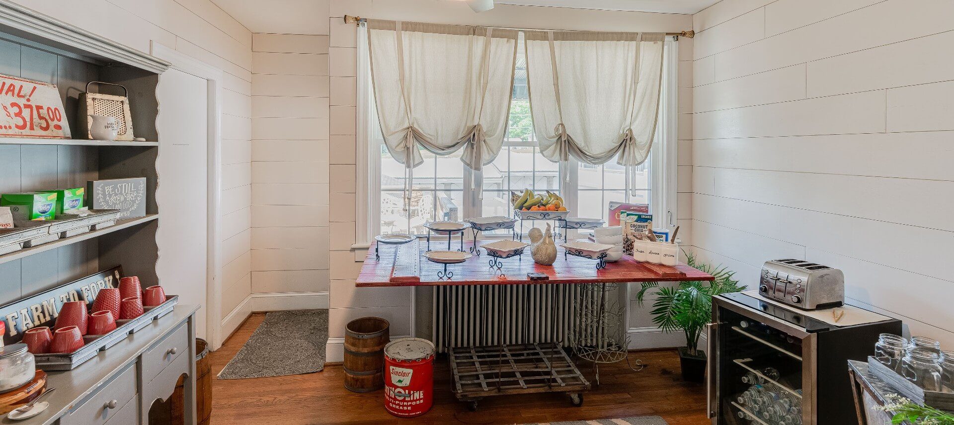 Dining area with white shiplap, table with buffet dishes and hutch with coffee mugs