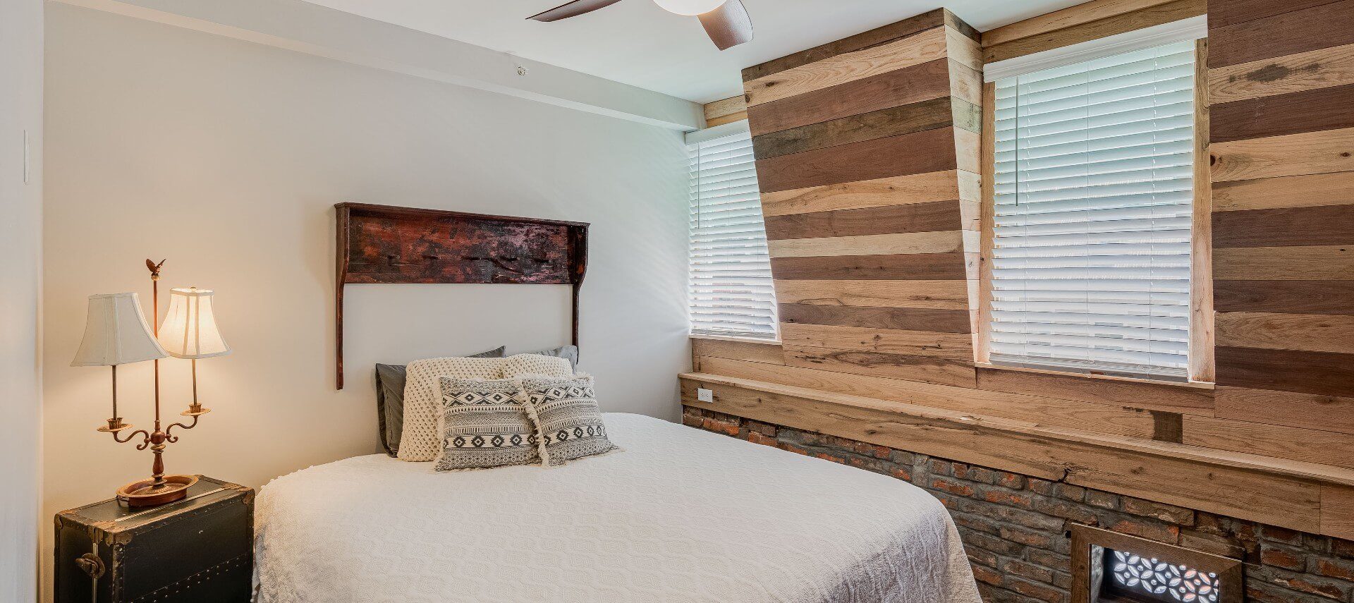 Bedroom with king bed, unique angled walls with rustic wood paneling and side table with lamp